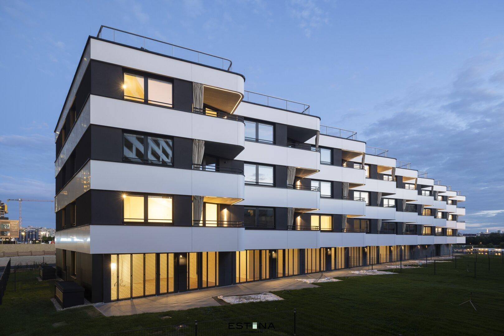 Moderne Wohnanlage mit gestuften Balkonen und großen Fenstern bei Abenddämmerung.