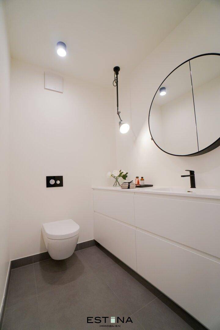 Modernes Gäste-WC mit wandhängender Toilette, Einzelwaschbecken und einem runden Wandspiegel.