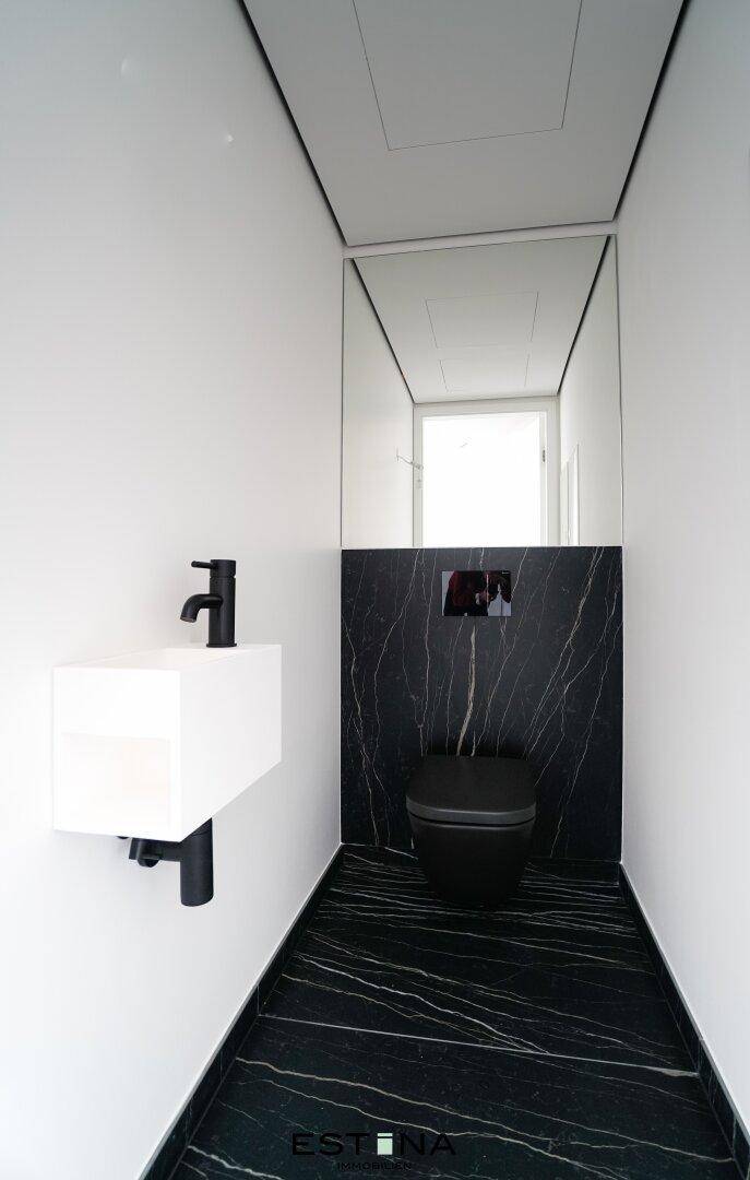Elegantes Gäste-WC mit schwarzen Marmorfliesen, wandhängender Toilette und modernem Waschbecken.