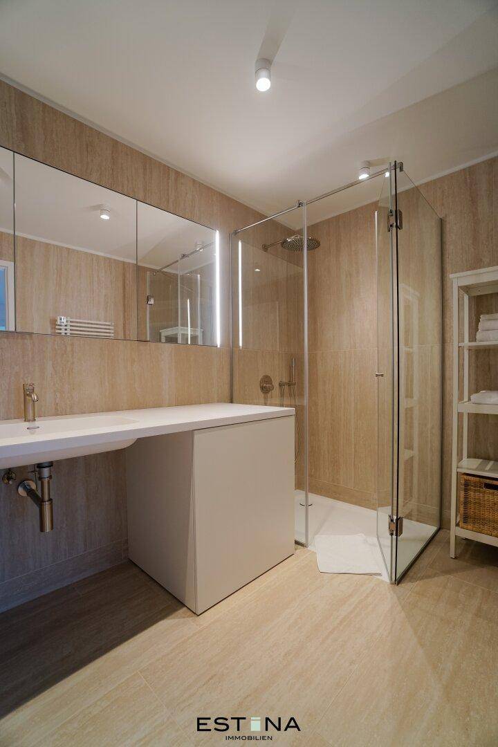 Elegantes Badezimmer mit beigefarbenen Fliesen, Glasdusche und modernem Waschtisch.