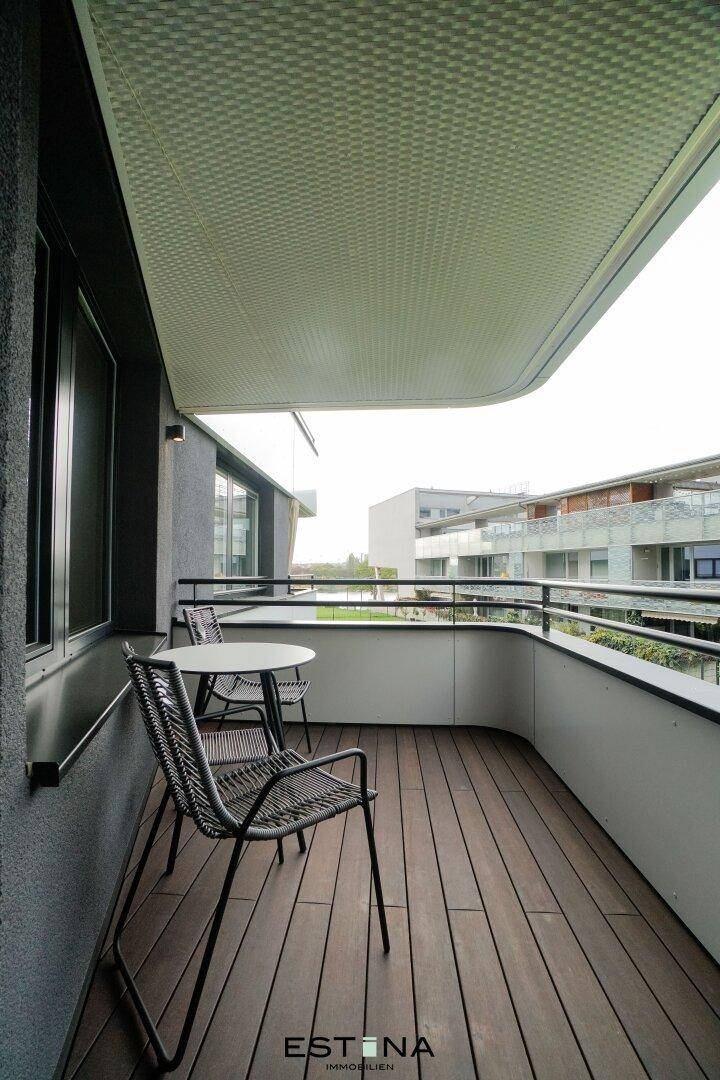 Geräumiger Balkon mit Holzdielen und moderner Bestuhlung, umgeben von weiteren Gebäuden.