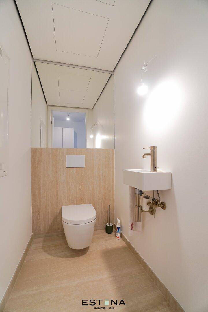 Modernes Gäste-WC mit wandhängender Toilette, kleinem Waschbecken und Spiegelfläche.