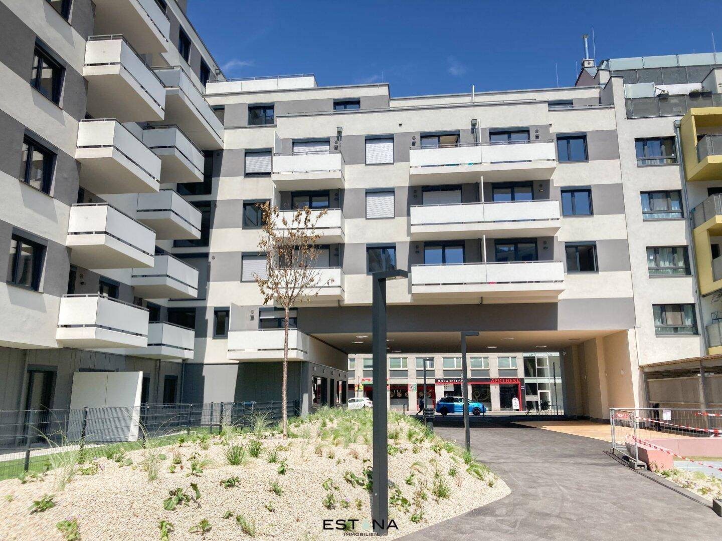 Moderner Wohnkomplex mit mehreren Balkonen, begrüntem Innenhof und architektonischen Durchgängen.