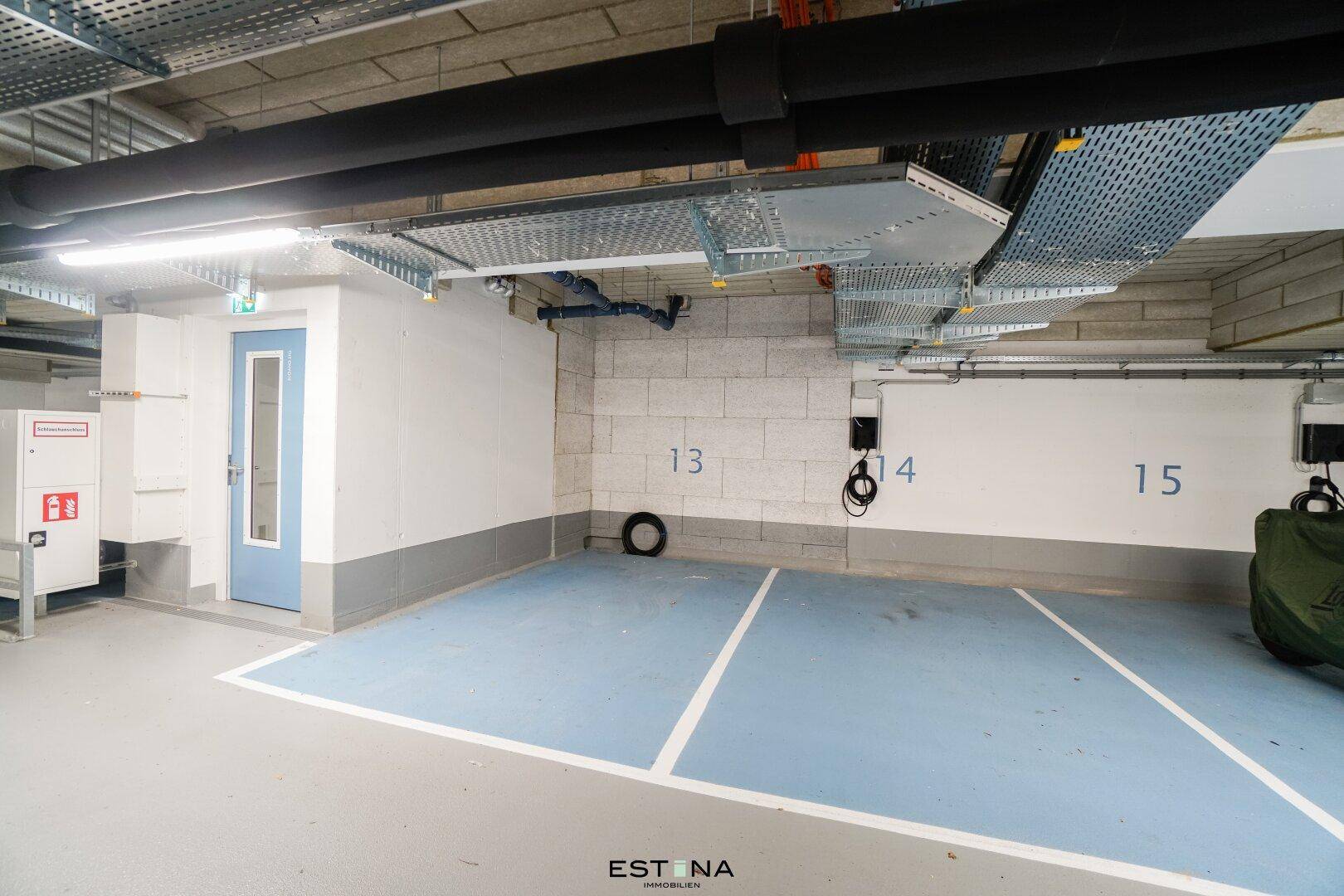 Einzelner Stellplatz in der Tiefgarage mit Zugangstür und sichtbaren technischen Installationen.