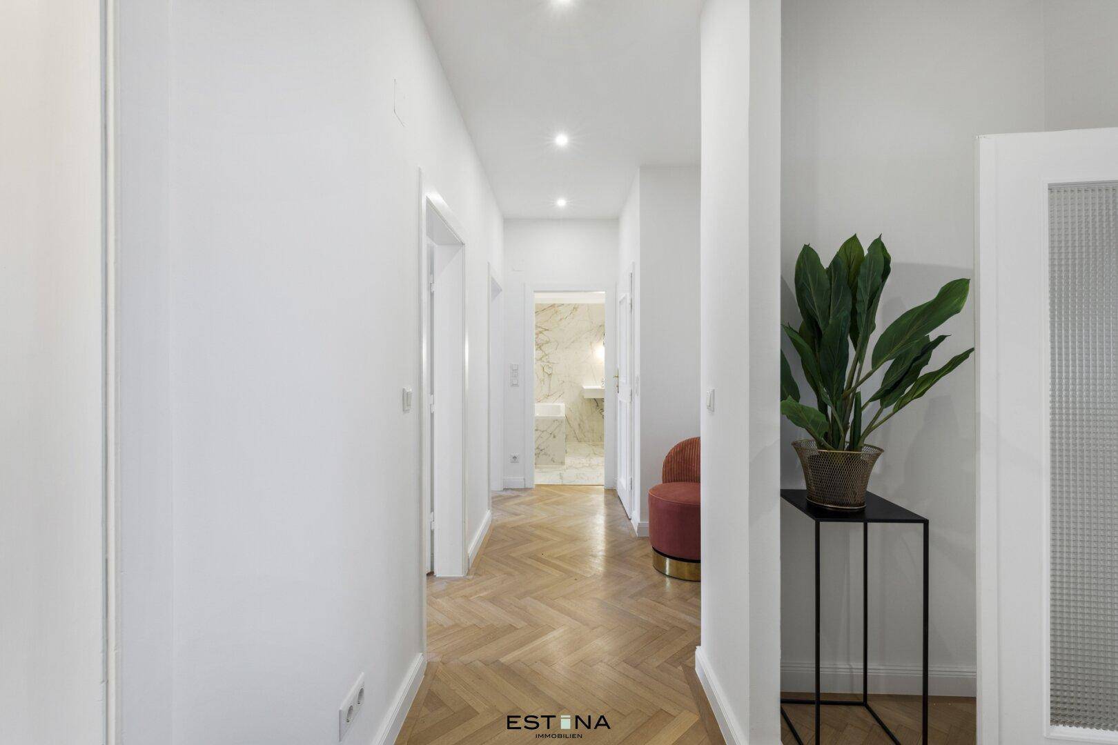 Heller Flur mit Fischgrätparkettboden und Blick auf das moderne Badezimmer.