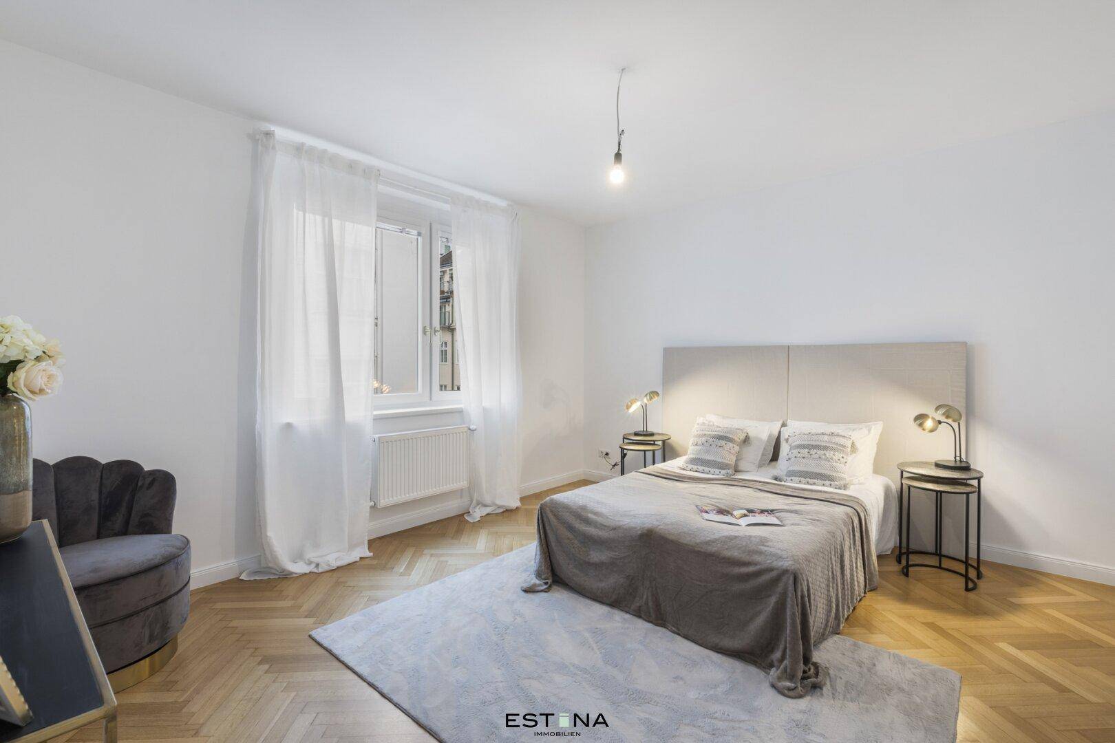 Helles Schlafzimmer mit Doppelbett, Nachttischen und großem Fenster mit Vorhängen.
