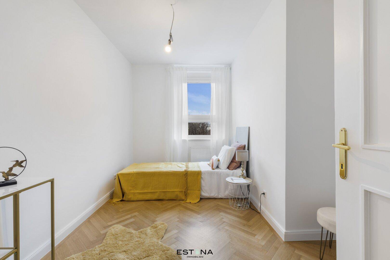 Helles Schlafzimmer mit Einzelbett, Fenster und Fischgrätparkettboden.