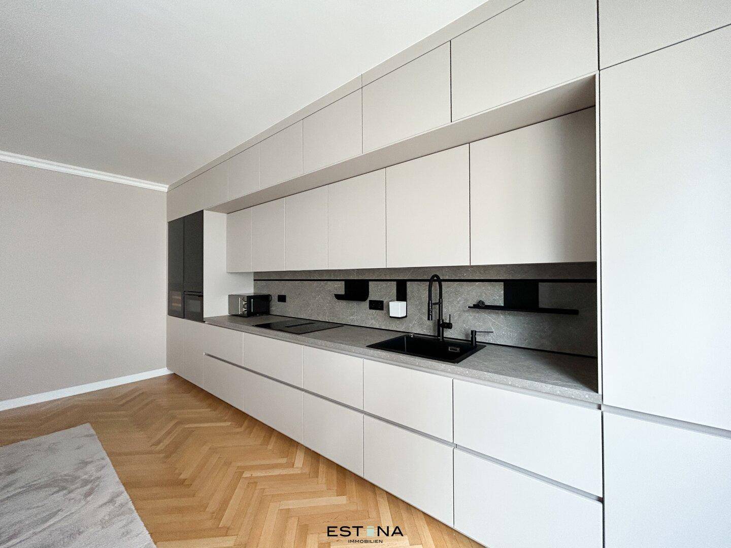 Schlanke, moderne Küche mit hellen Schränken, dunkler Arbeitsplatte und integrierten Geräten.