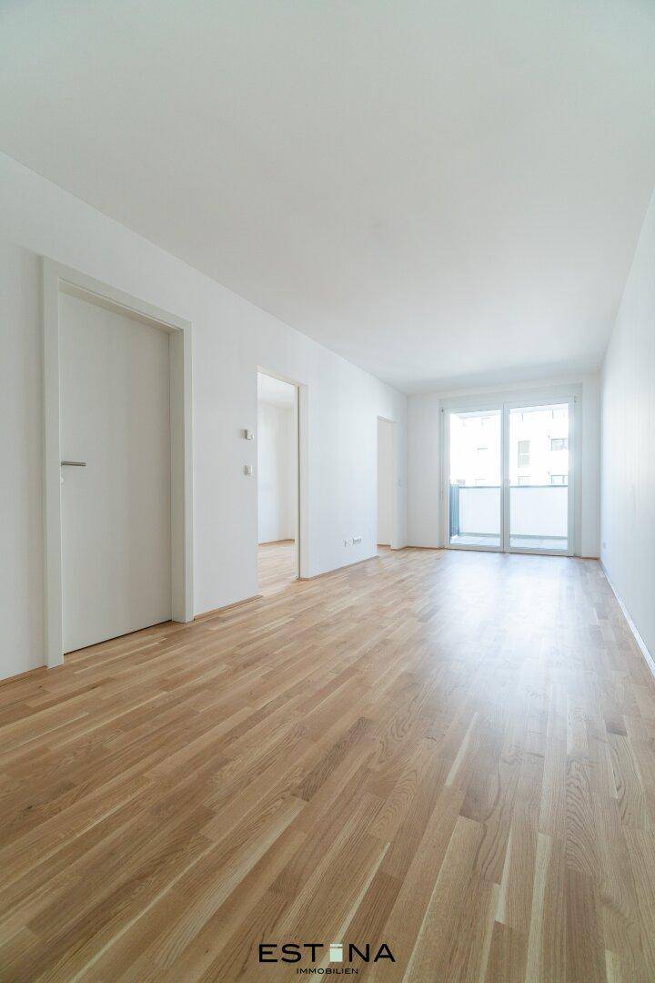 Geräumiger, heller Wohnbereich mit Parkettboden und Zugang zum Balkon durch große Fenster.