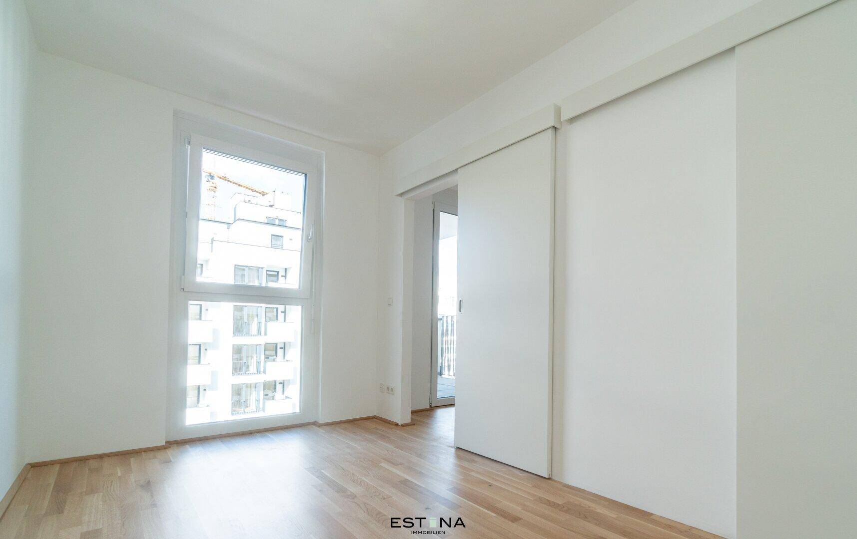 Helles Zimmer mit großem Fenster und Zugang zu einem Außenbereich, ideal als Schlafzimmer.