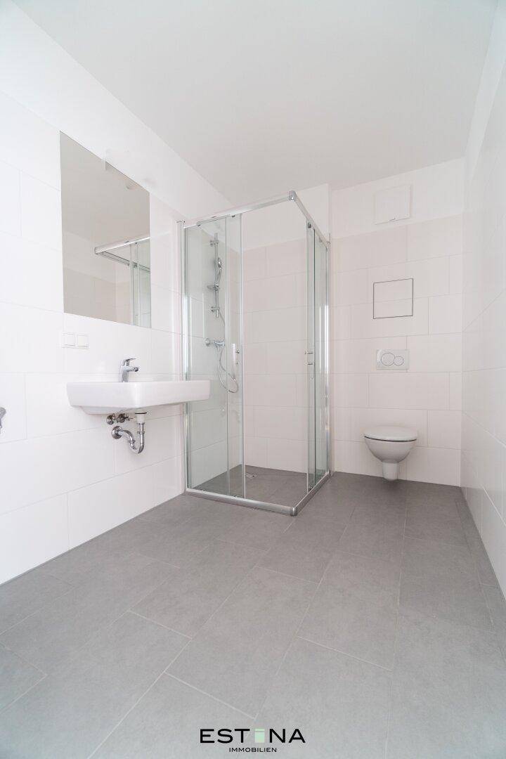 Modernes Badezimmer mit grauen Fliesen, Duschkabine und wandhängendem WC in Weiß.