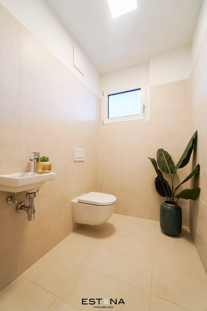 Kleines Gäste-WC mit Fenster, Wand-WC und Waschbecken in hellen Beigetönen.