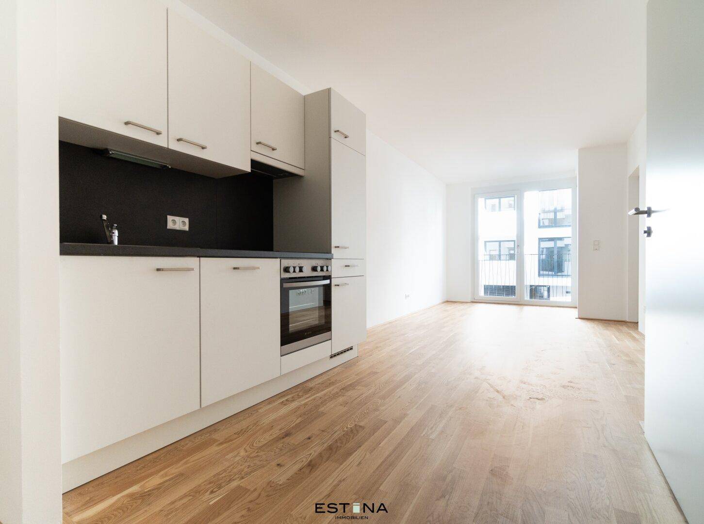 Moderne Küchenzeile mit weißen Schränken, dunkler Arbeitsplatte und integriertem Backofen.