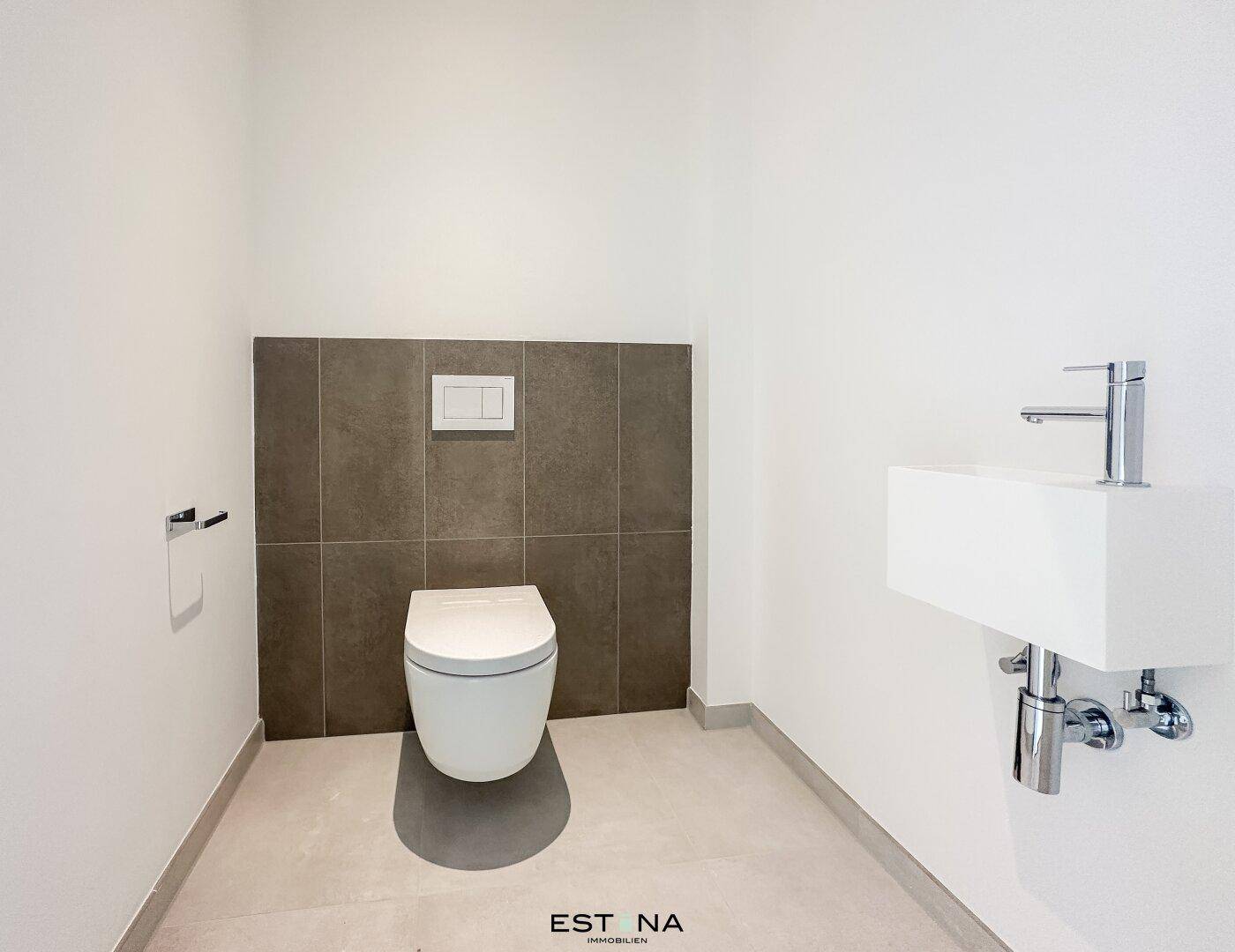 Modernes Gäste-WC mit Wand-WC, kleinem Waschbecken und eleganten Fliesen in neuwertigem Zustand.