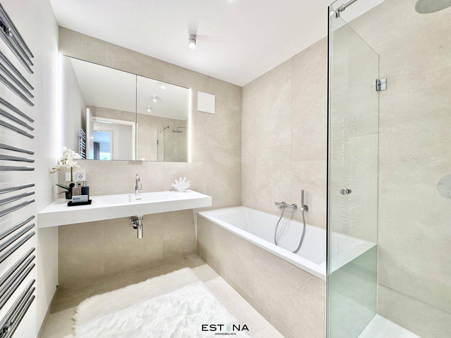 Modernes Badezimmer mit Badewanne, ebenerdiger Dusche und beheiztem Handtuchhalter in Beige.