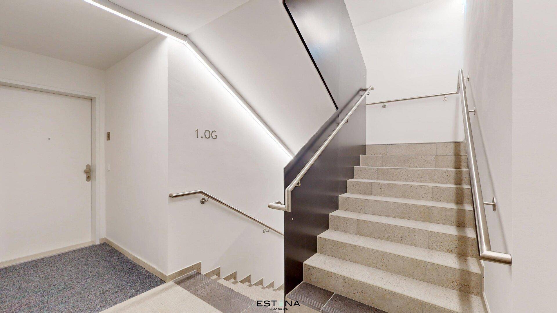 Modernes Treppenhaus mit Steinstufen und Edelstahlgeländer, gut beleuchtet.