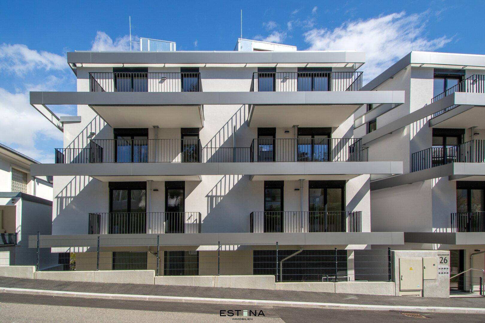 Nahaufnahme der modernen Fassade eines Neubaus mit mehreren Balkonen und großen Fensterfronten.