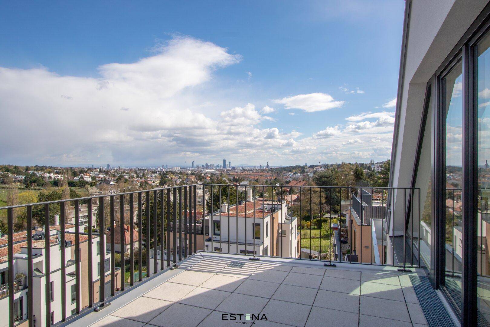 Großer Balkon mit Stadtblick und umliegender grüner Landschaft unter blauem Himmel.