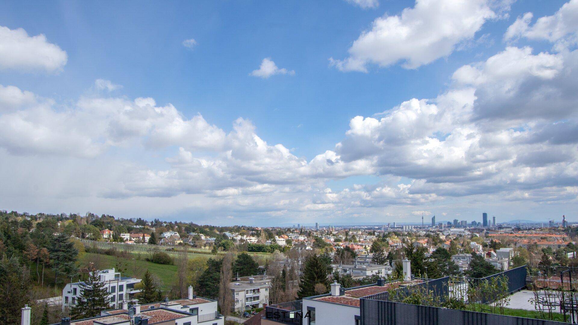 Weitläufiger Blick über die Stadt und die umliegende grüne Landschaft unter einem bewölkten Himmel.