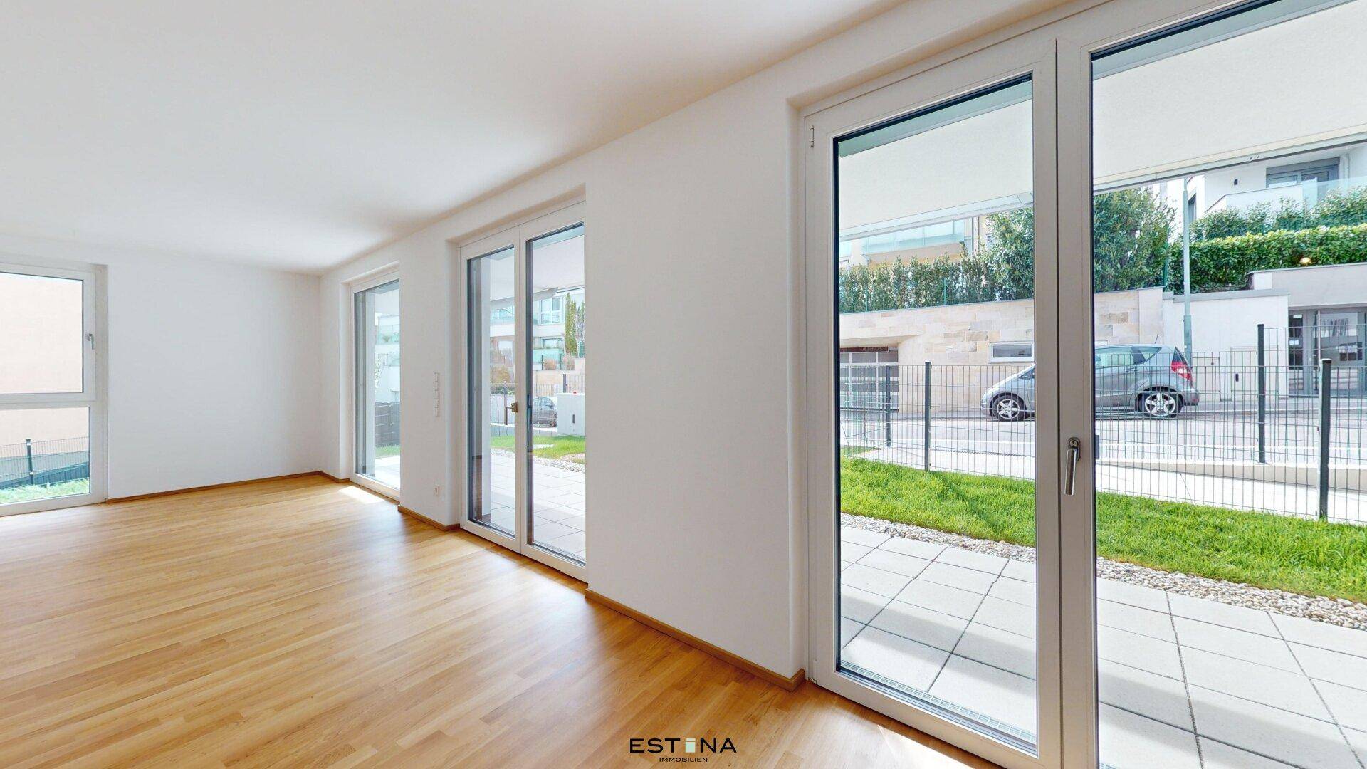 Heller Wohnraum mit Holzboden und großen Fensterfronten, die Zugang zu einem Außenbereich bieten.