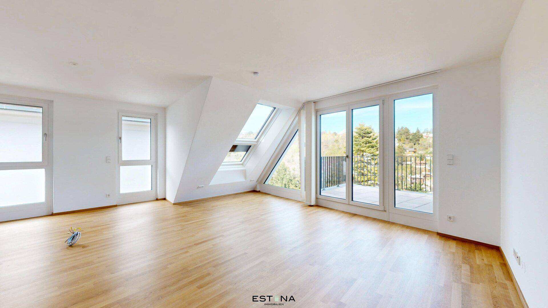 Geräumiger Wohnbereich mit Holzboden, großen Fenstern und Dachschrägen, bietet viel natürliches Licht.