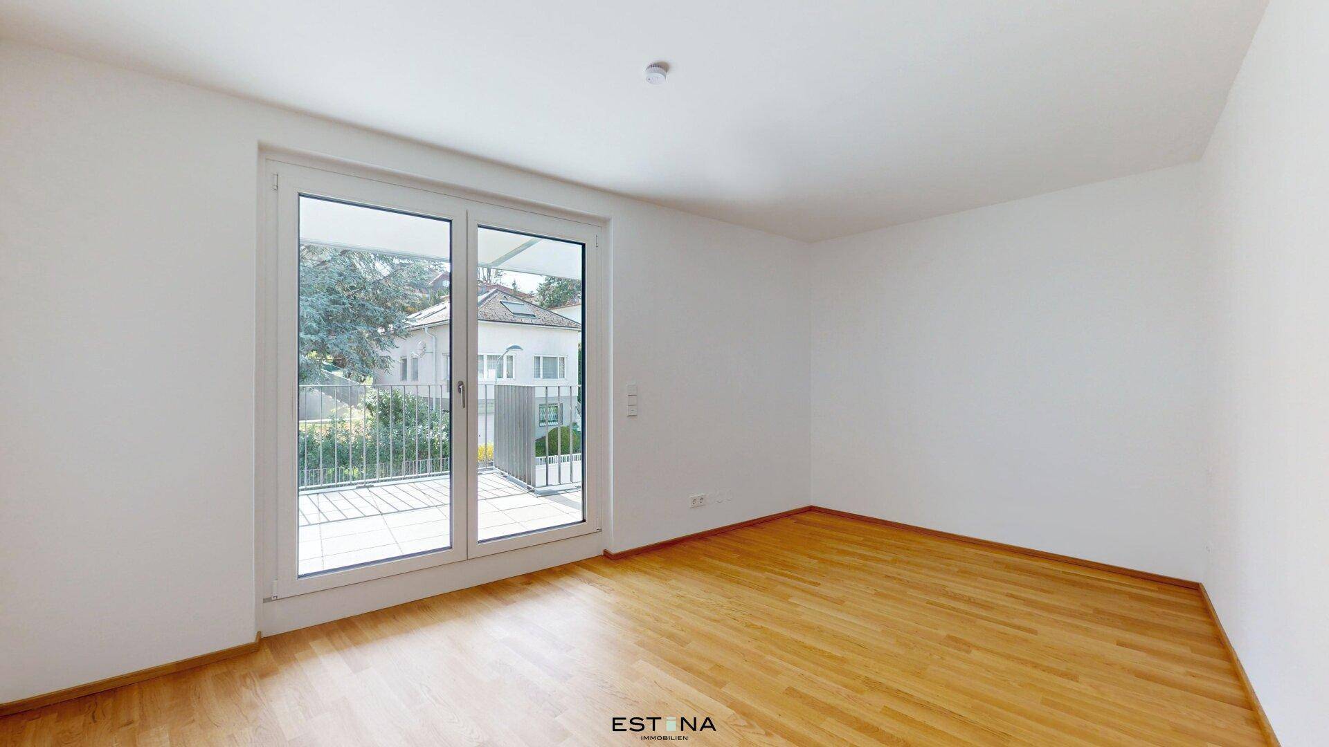 Leerer Raum mit Holzboden und einer großen Balkontür, die viel Licht hereinlässt.