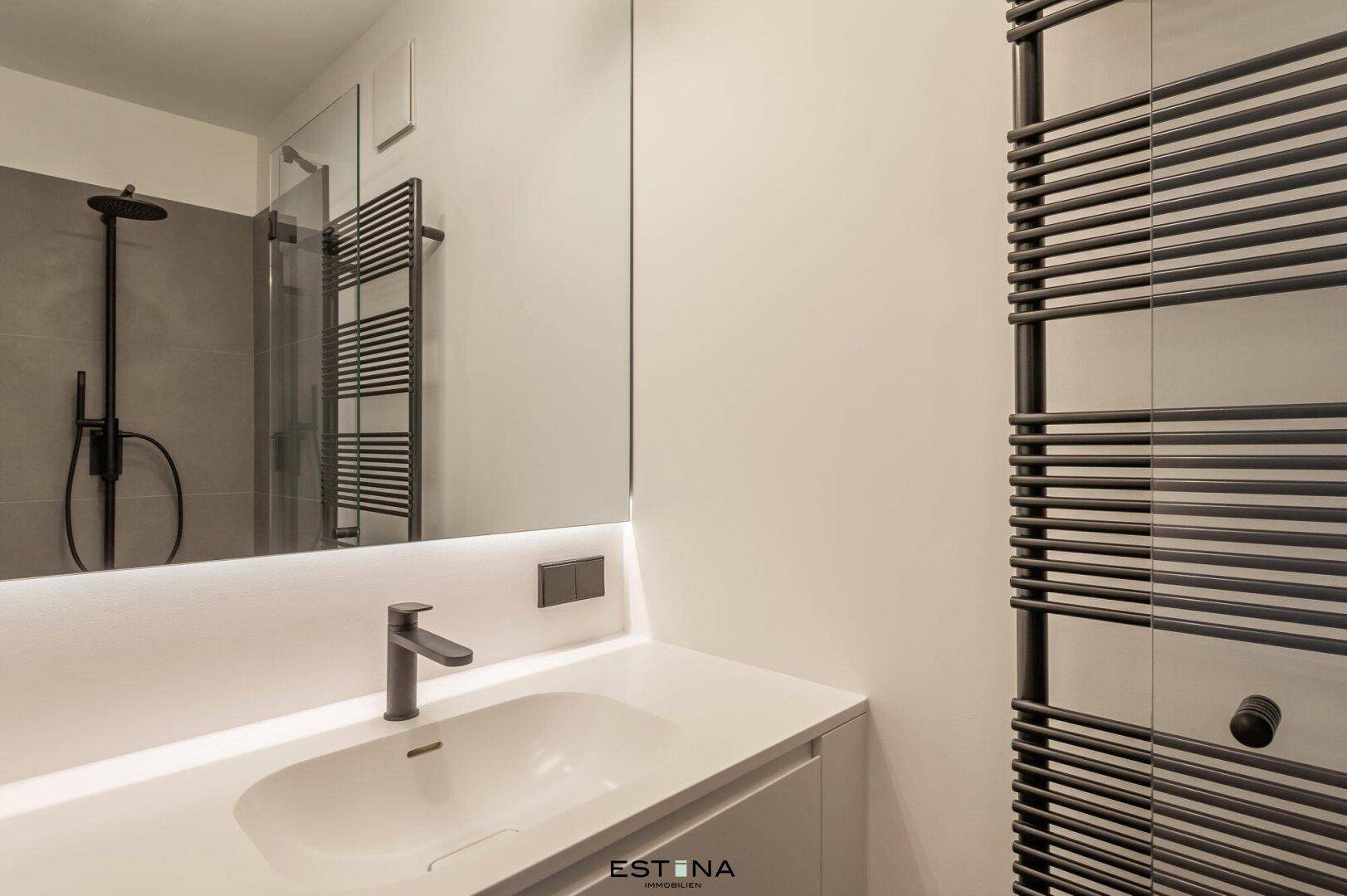 Modernes Badezimmer mit Einzelwaschbecken, beleuchtetem Spiegel und Handtuchheizkörper.