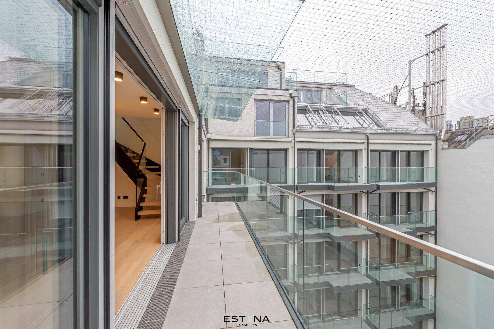 Langer Balkon mit Glasgeländer und Blick auf die umliegenden Gebäude.