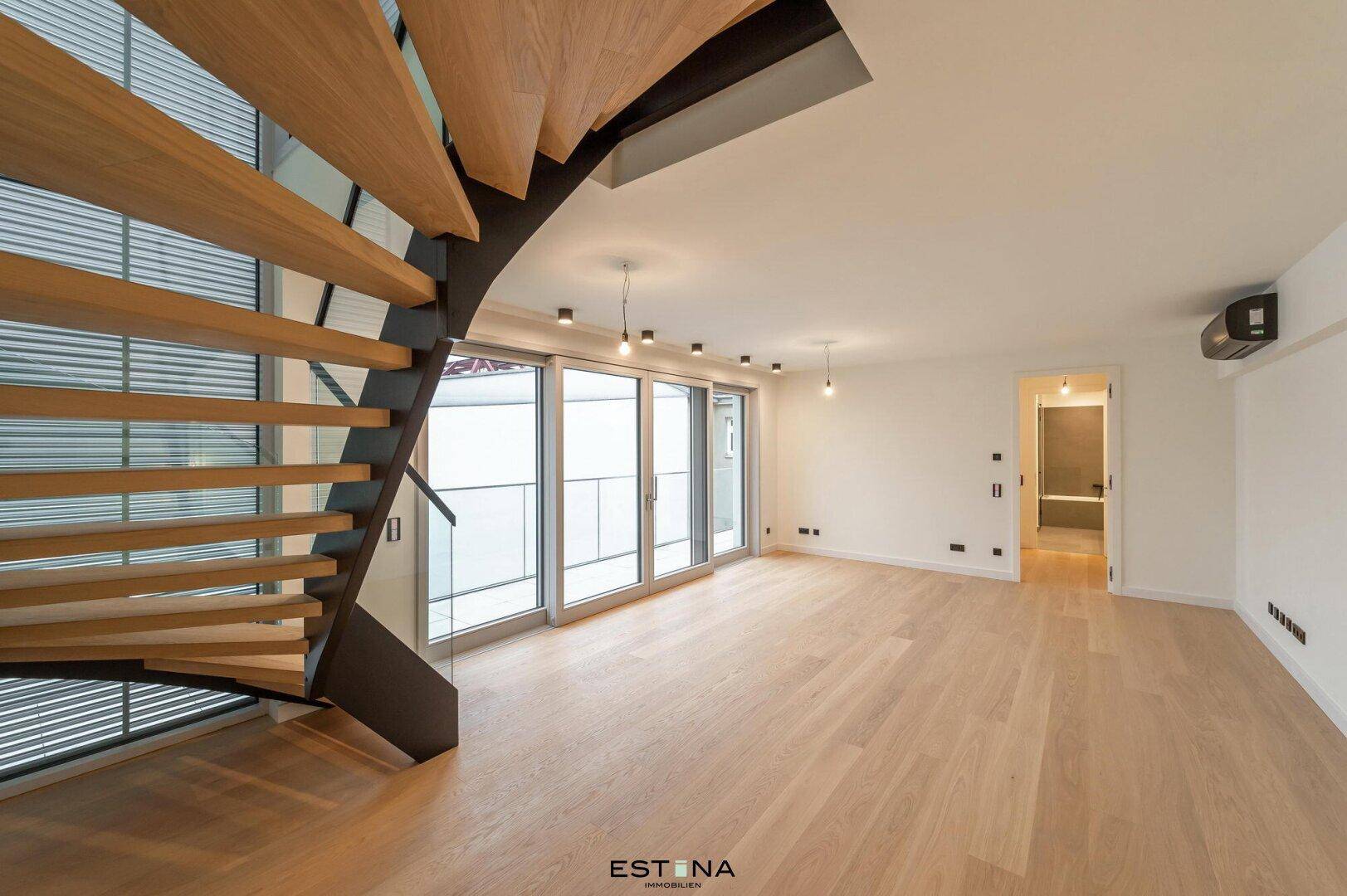 Geräumiges Wohnzimmer mit elegantem Holzparkett und einer modernen Holztreppe.