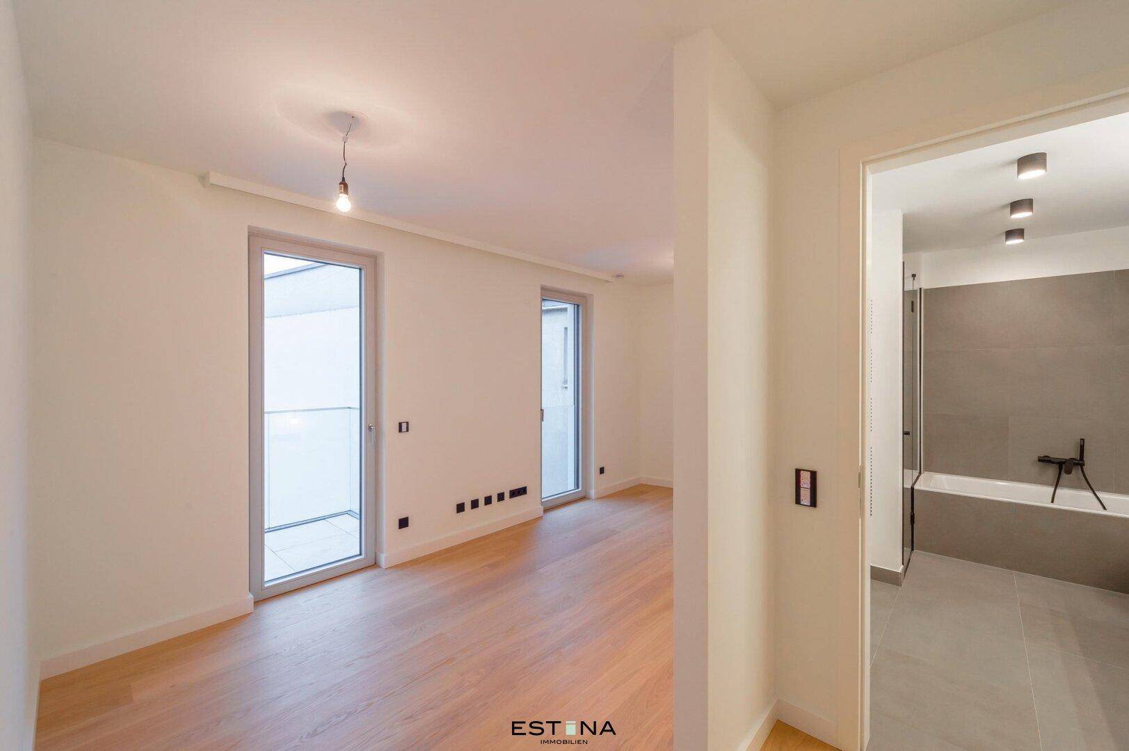 Helles Schlafzimmer mit Parkettboden und Zugang zu einem modernen Badezimmer.