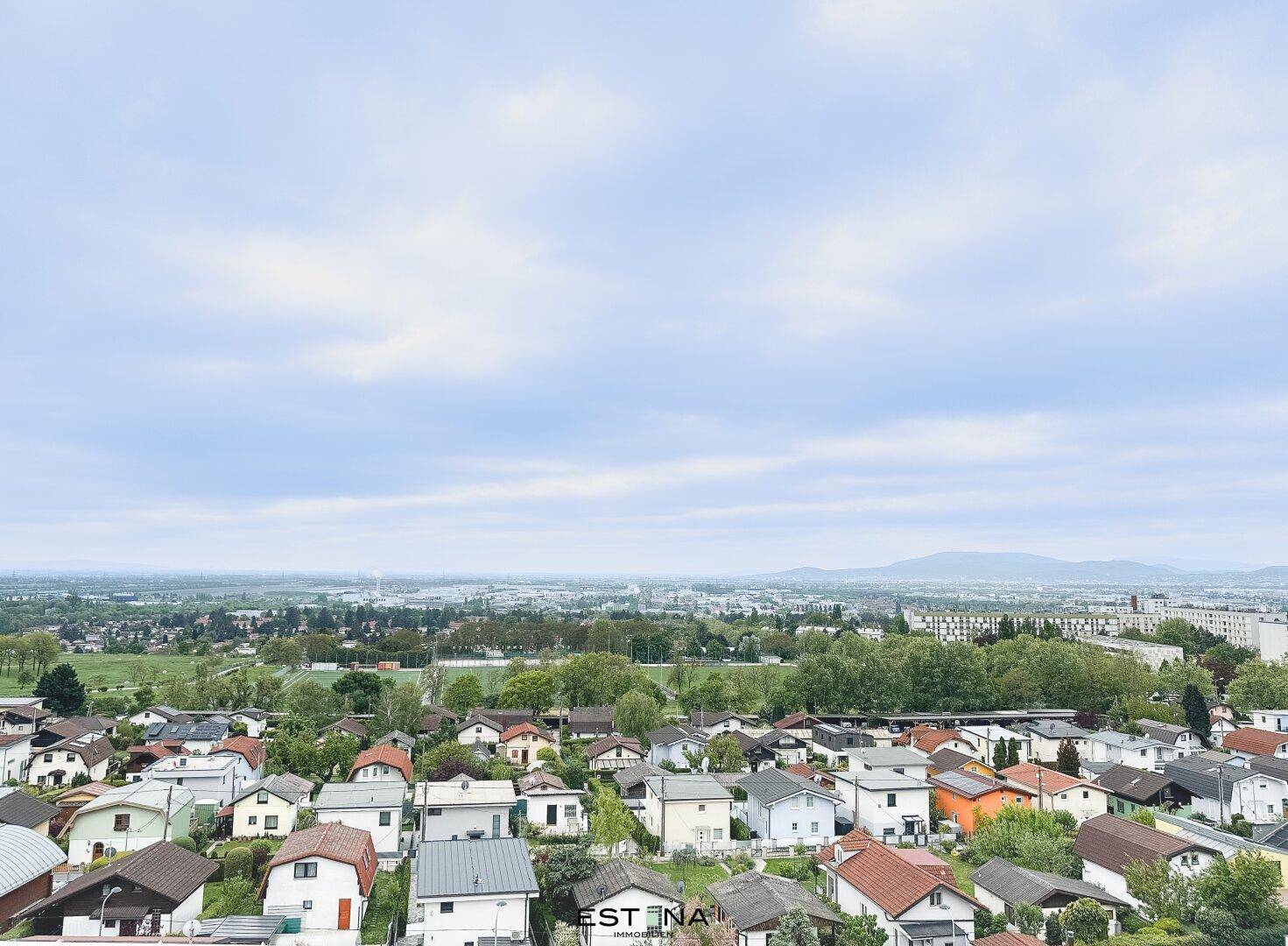 Weitläufiger Blick über eine Wohnsiedlung mit viel Grün und Bergen am Horizont.