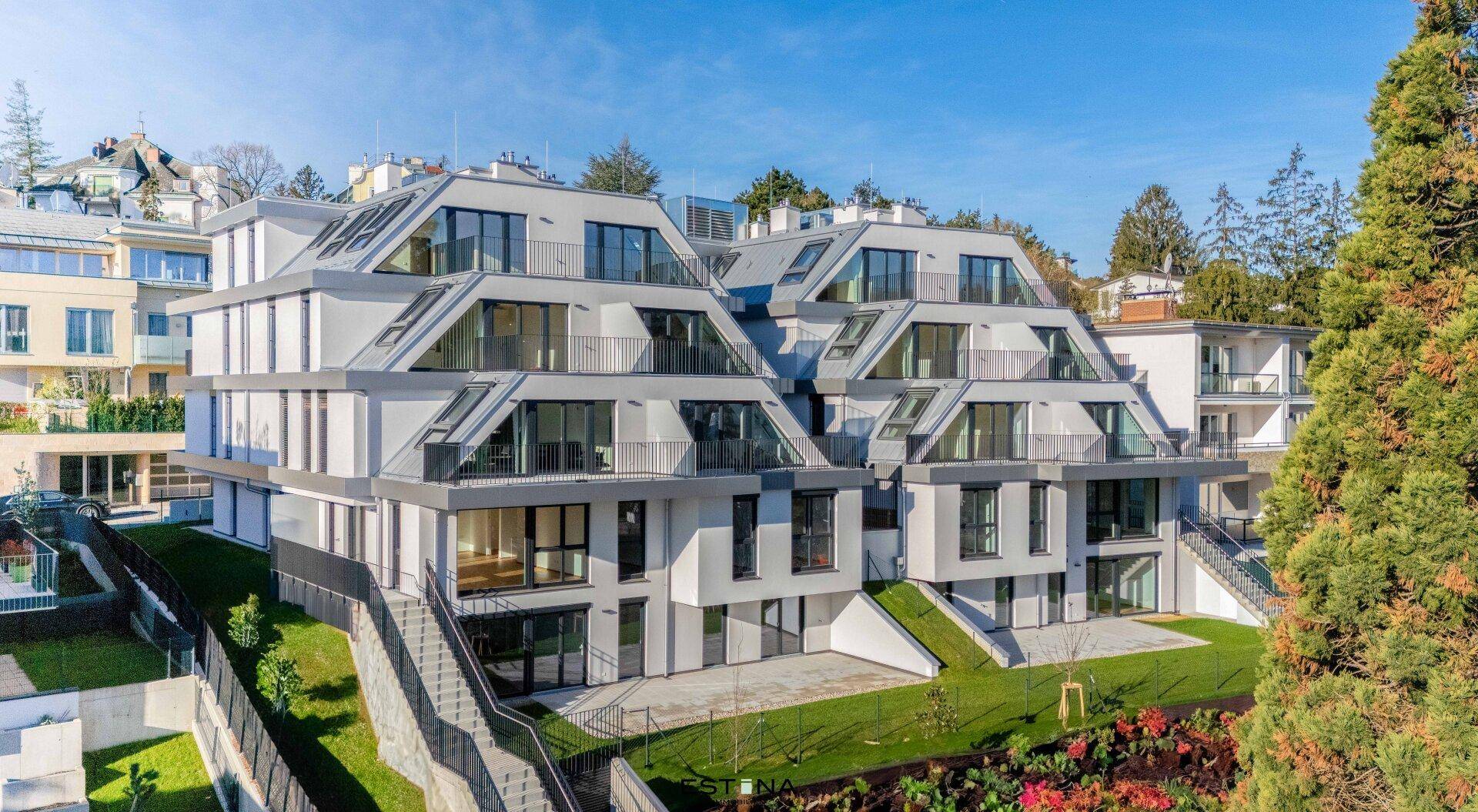 Modernes Mehrfamilienhaus mit gestufter Architektur, großen Fensterfronten und Balkonen in grüner Umgebung.