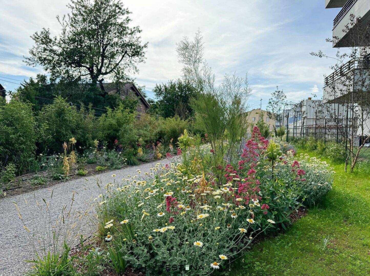 Ein idyllischer Gartenweg schlängelt sich durch blühende Blumenbeete unter einem bewölkten Himmel.