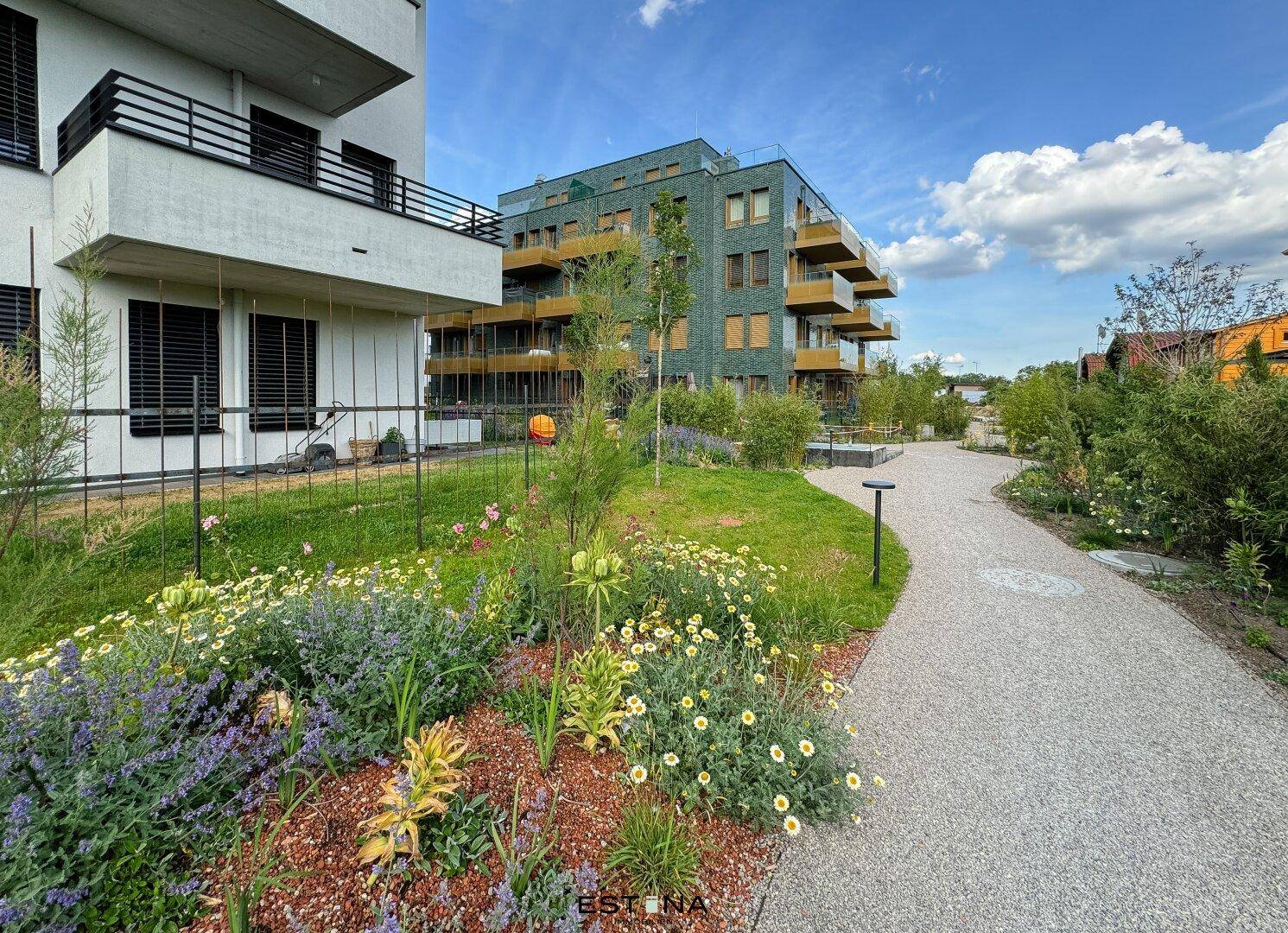 Angelegter Gartenbereich mit Gehwegen, Blumenbeeten und modernen Wohngebäuden im Hintergrund.