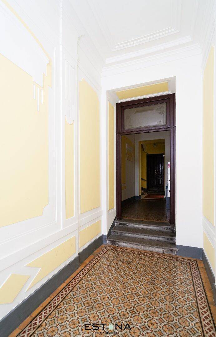 Historischer Eingangsbereich mit gemustertem Fliesenboden und hohen Decken, der zum Treppenhaus führt.