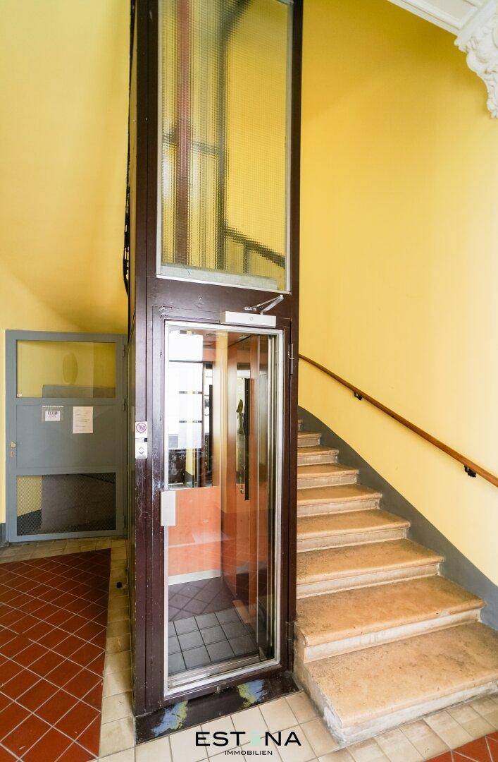 Treppenhaus mit historischem Charme und einem modernen Aufzug für barrierefreien Zugang zu den Etagen.