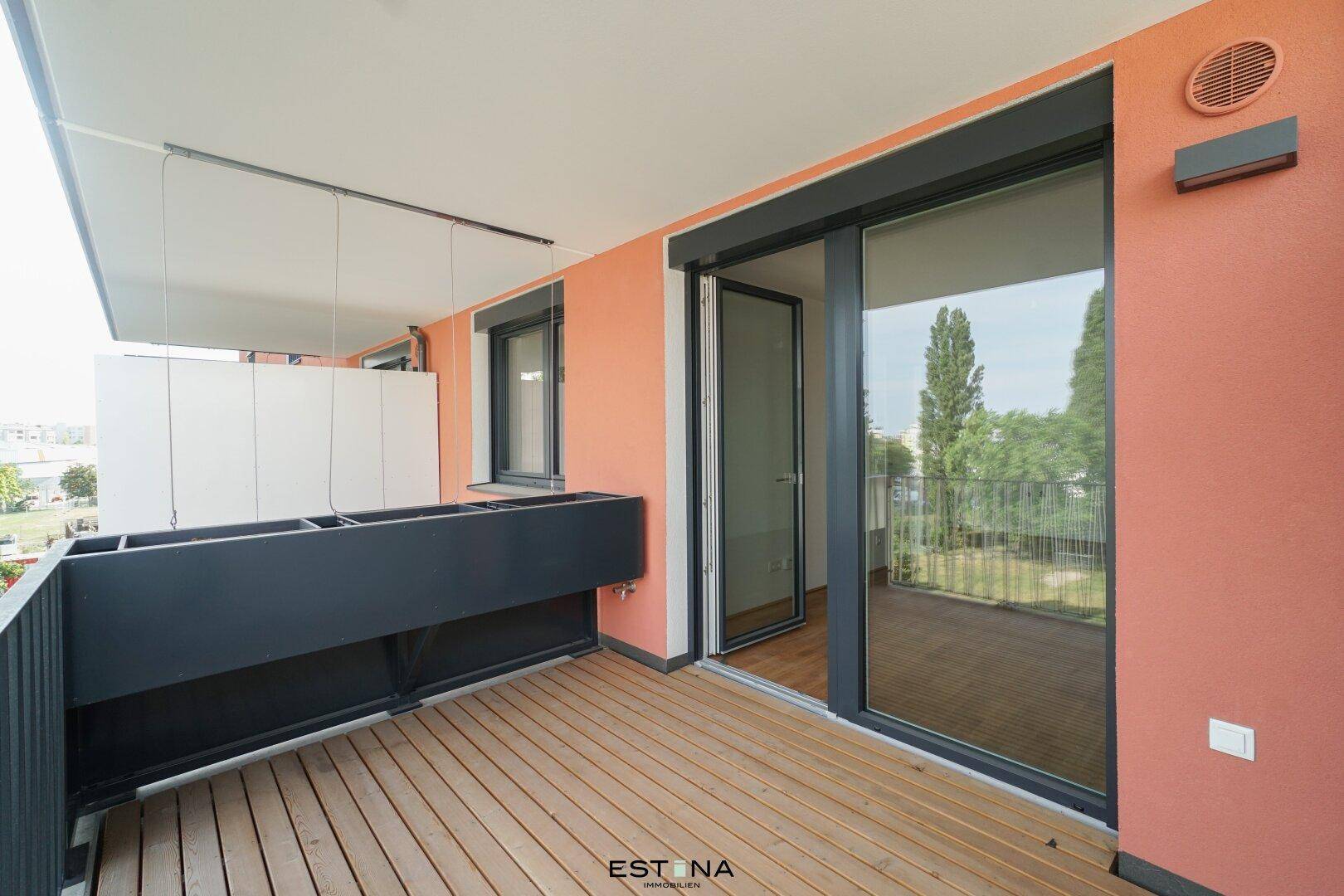 Moderner Balkon mit Holzboden und Schiebetürzugang, umgeben von einer orangefarbenen Fassade.