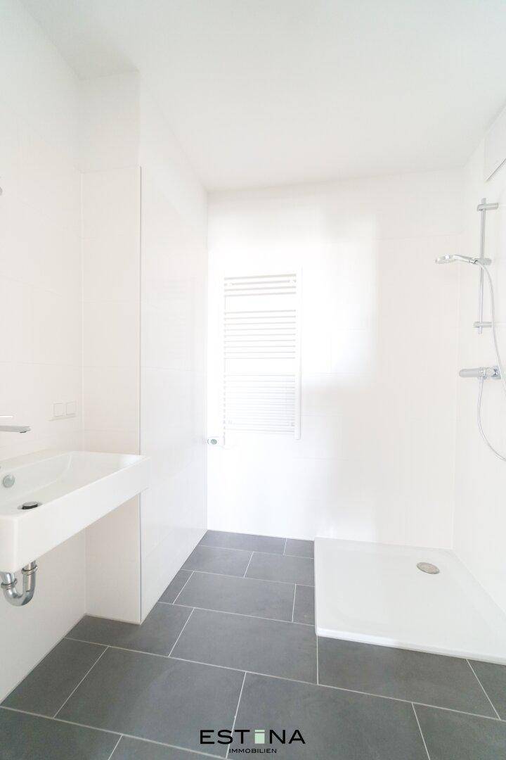 Modernes Badezimmer mit grauen Bodenfliesen, weißer Wandverkleidung und ebenerdiger Dusche.