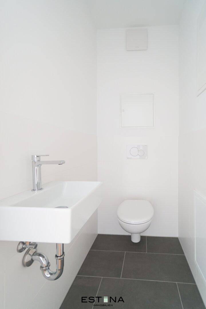 Modernes Gäste-WC mit grauen Bodenfliesen, wandhängendem WC und elegantem Waschbecken.
