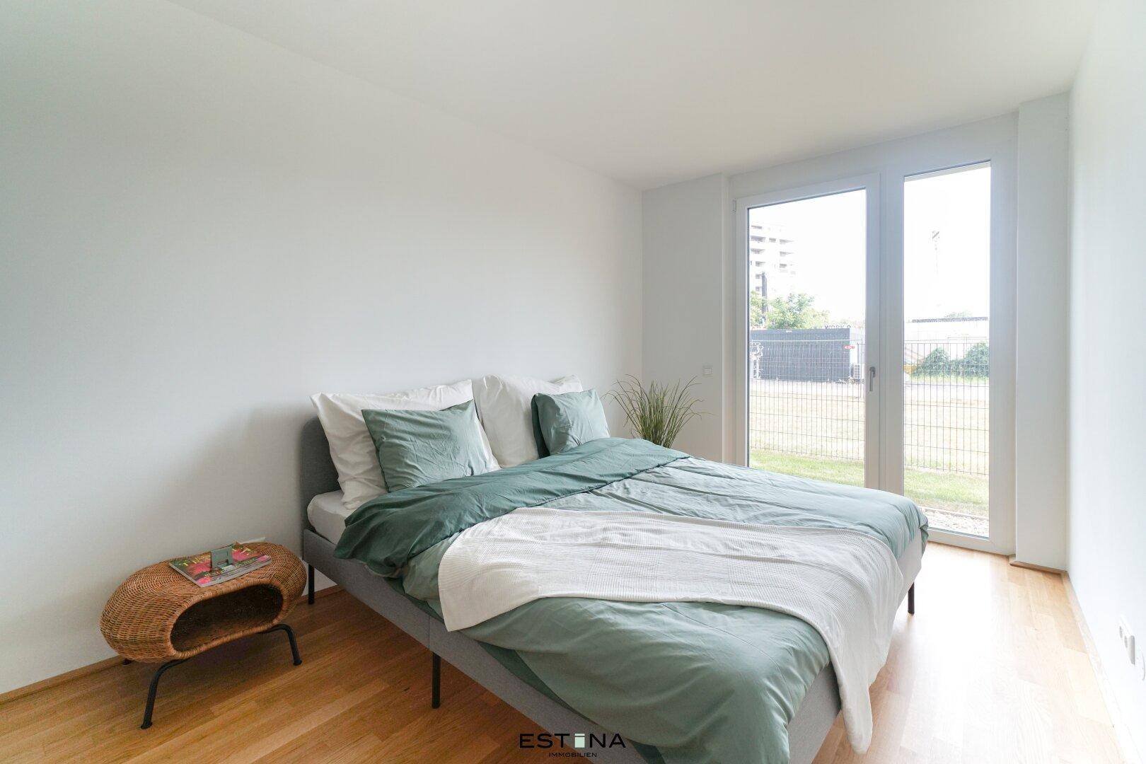 Helles Schlafzimmer mit Holzboden und direktem Zugang zu einer kleinen Grünfläche.