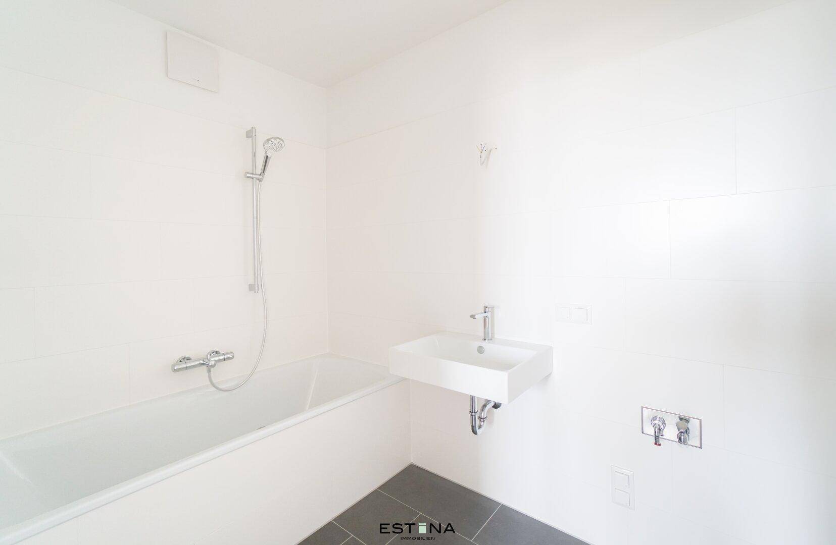 Modernes Badezimmer mit Badewanne, Duscharmatur, Einzelwaschbecken und grauen Bodenfliesen.