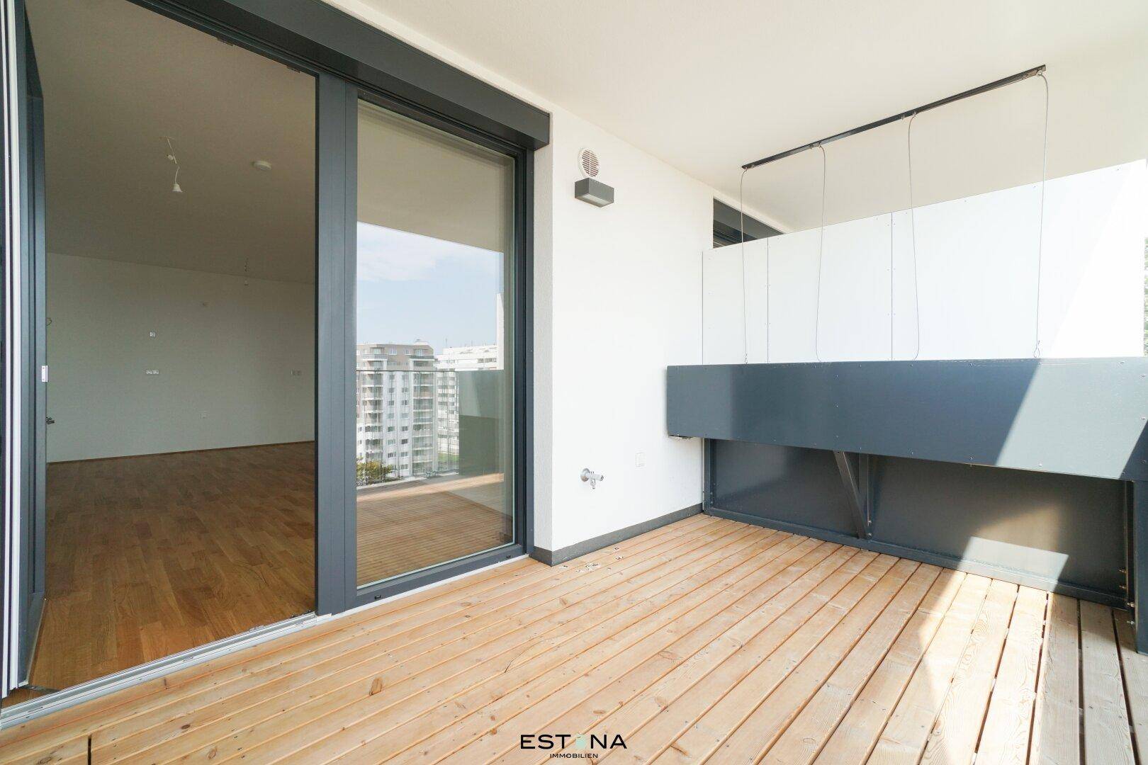 Geräumiger Balkon mit Holzboden und Schiebetür, bietet Zugang zu einem hellen Innenraum und Stadtblick.
