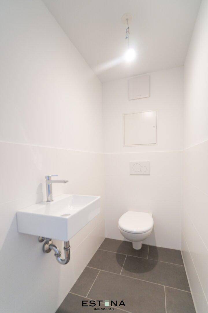 Funktionelles Gäste-WC mit wandhängender Toilette, Einzelwaschbecken und grauen Bodenfliesen.