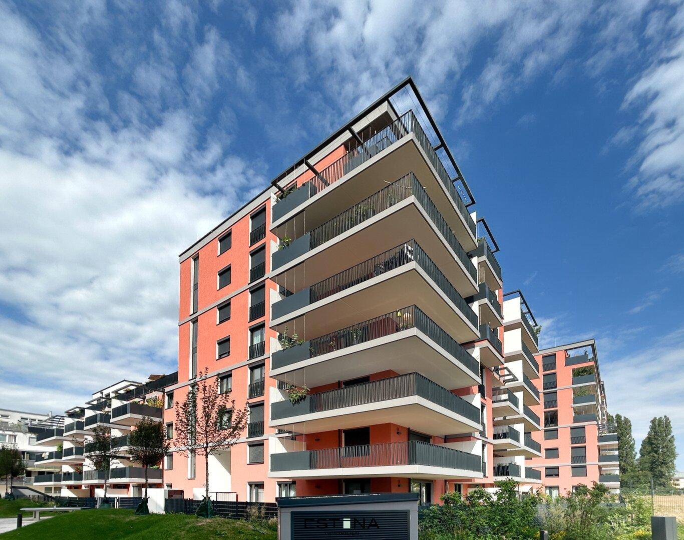 Modernes Wohngebäude mit lebhafter orangefarbener Fassade und zahlreichen Balkonen unter blauem Himmel.