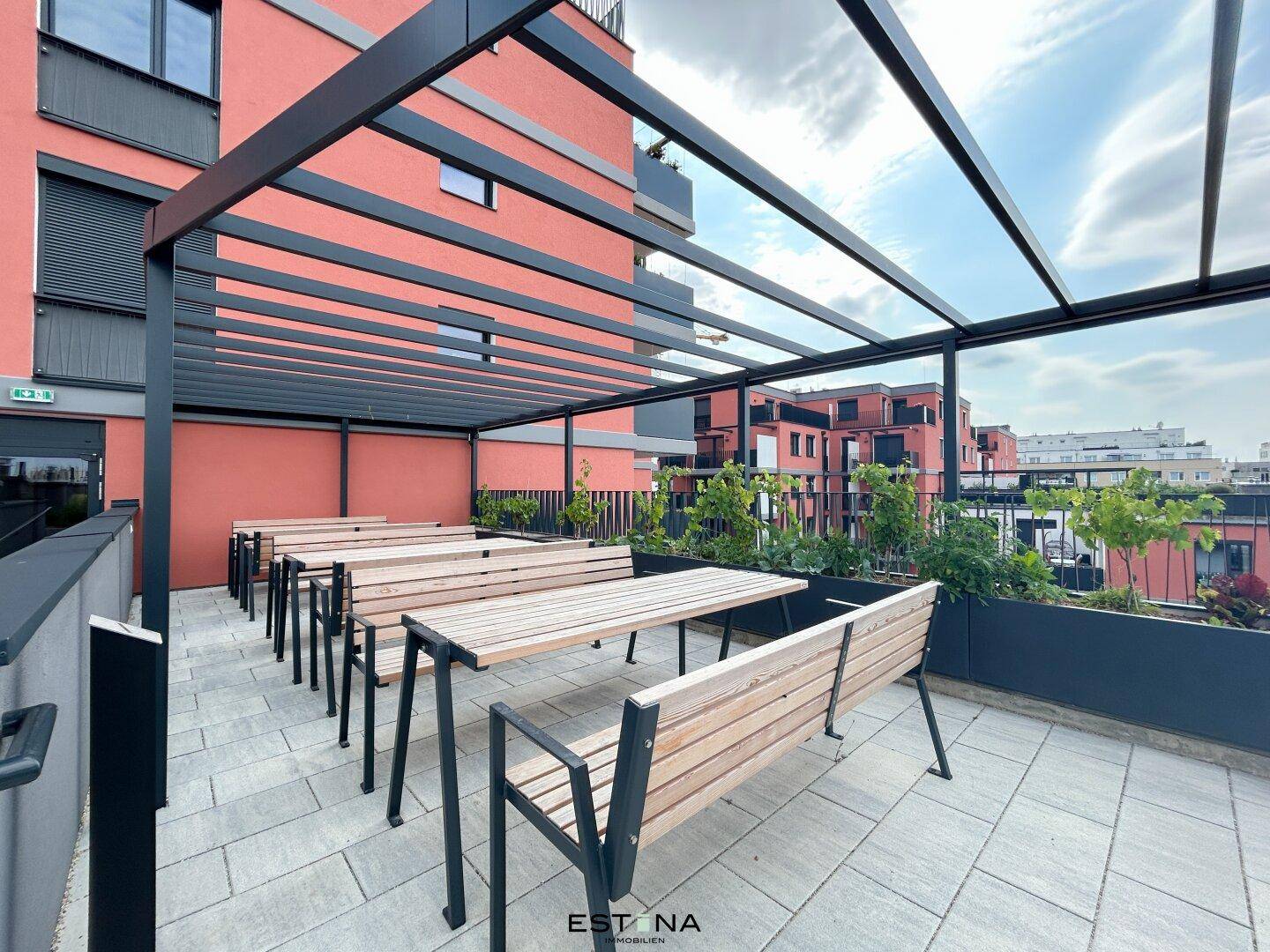 Gemeinschaftlicher Außenbereich mit Holztischen und Bänken unter einer Pergola, ideal zum Entspannen.