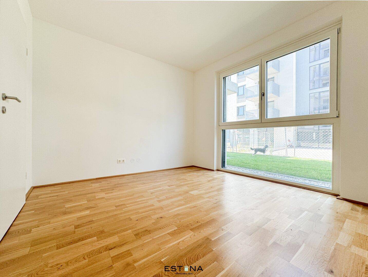 Helles Zimmer mit Parkettboden und bodentiefen Fenstern, Blick ins Grüne.