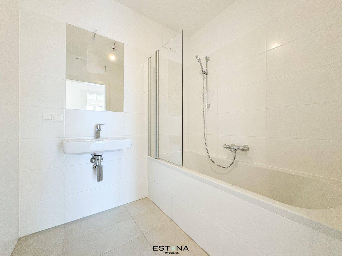 Modernes Badezimmer mit weißen Fliesen, Badewanne und Waschtisch, in neuwertigem Zustand.