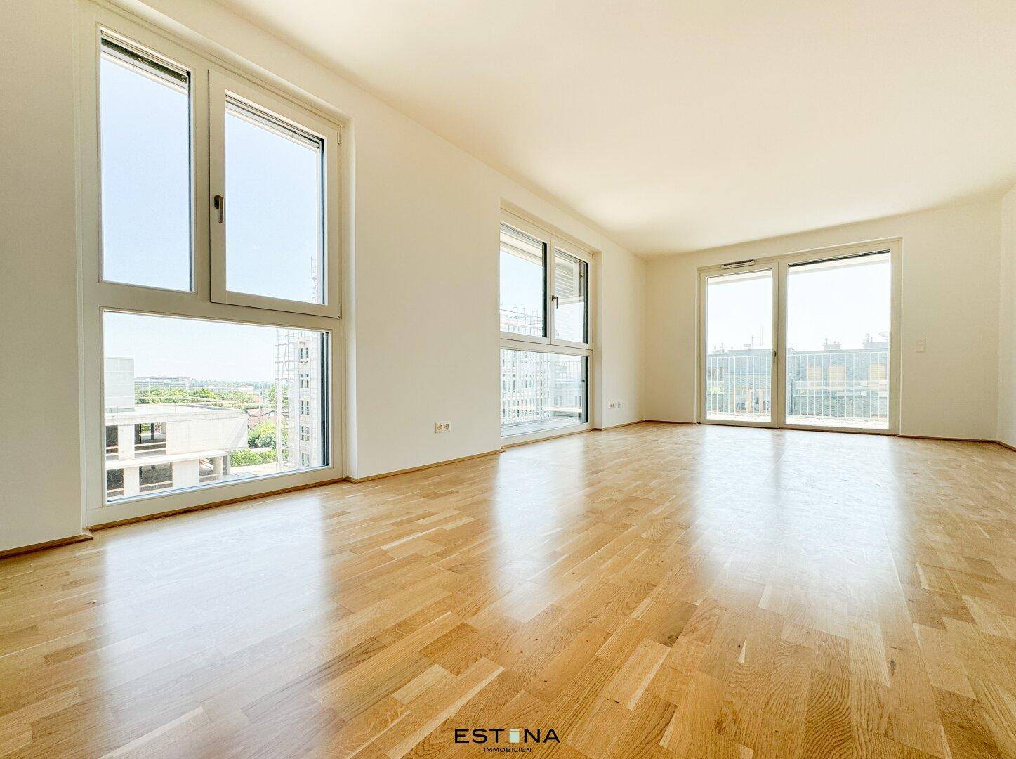 Geräumiges Wohnzimmer mit großen Fenstern und Zugang zu einem Balkon, viel Tageslicht.