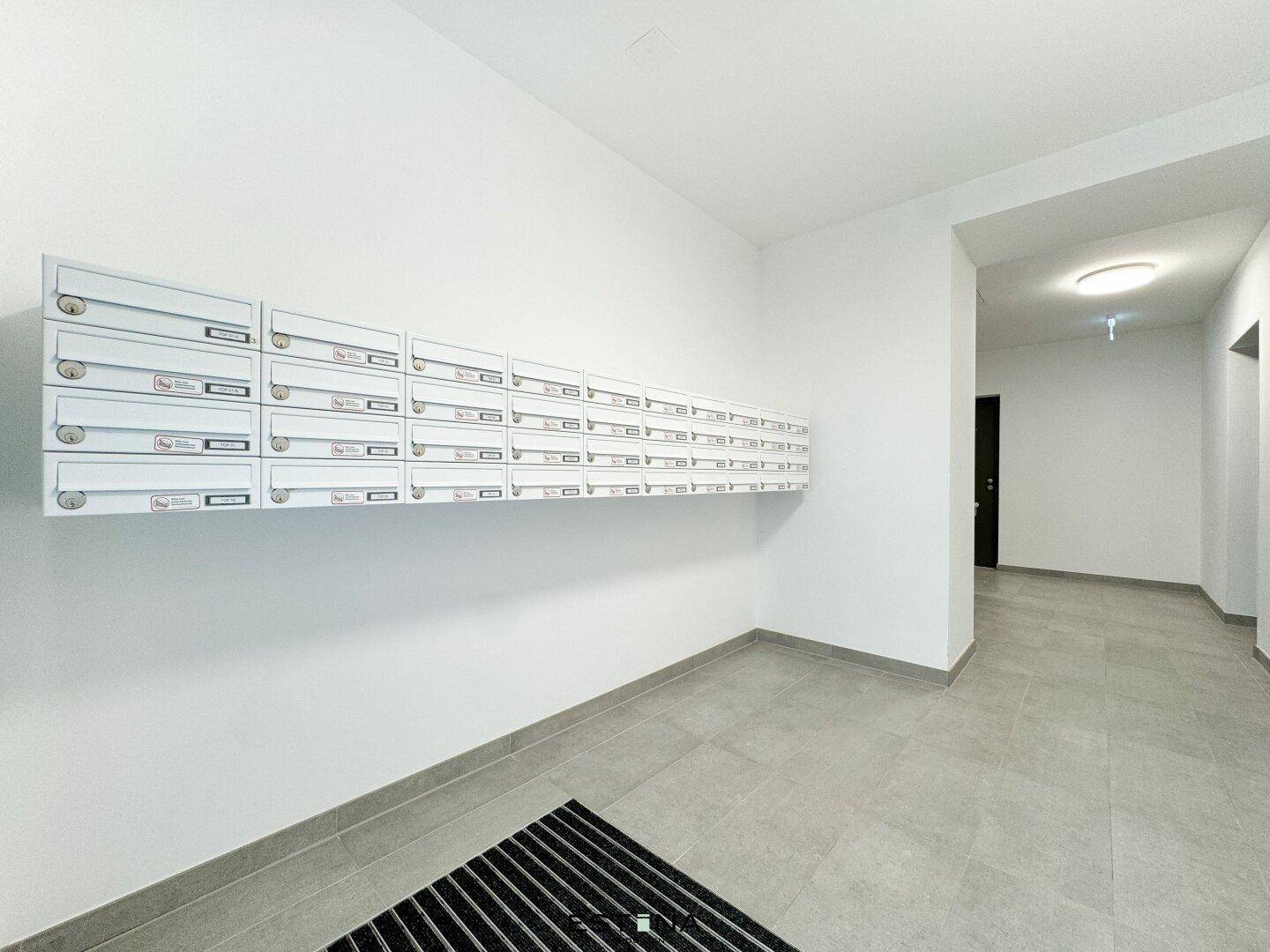 Heller Eingangsbereich mit Briefkästen an der Wand und modernen Fliesen.
