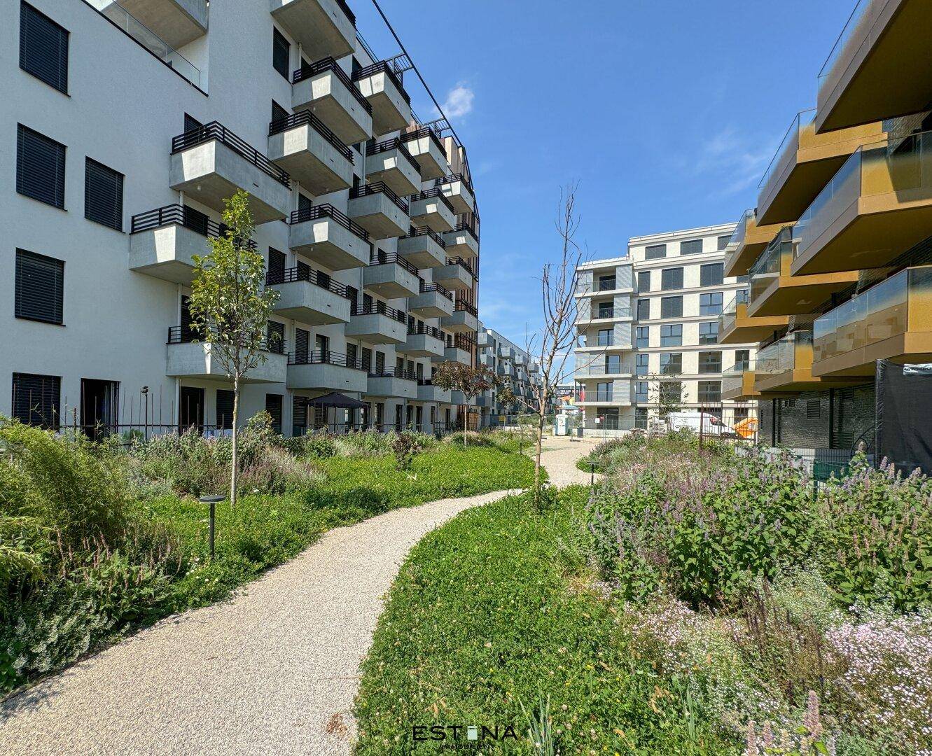Moderne Wohngebäude mit Balkonen und gepflegten Grünflächen unter blauem Himmel.
